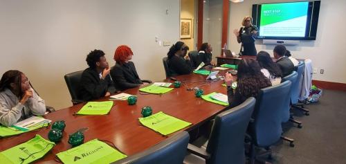 A group engaged in a meeting on financial literacy listens to a presenter, with bright green bags adorning the table.