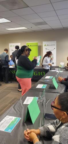 People engaging at a job fair, exploring brochures under a REGIONS banner promoting financial literacy.