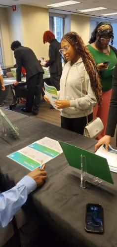 People engaging at a job fair, discussing financial literacy while reading brochures and filling out forms at tables.