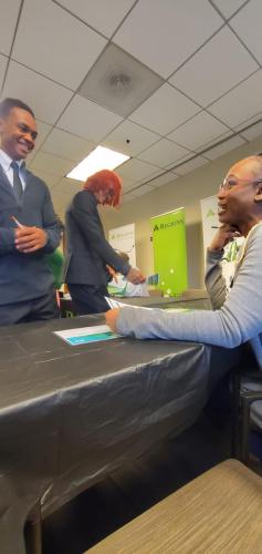 Three people in a professional setting with Region banners discuss financial literacy; one is seated at a table, engaging with others.