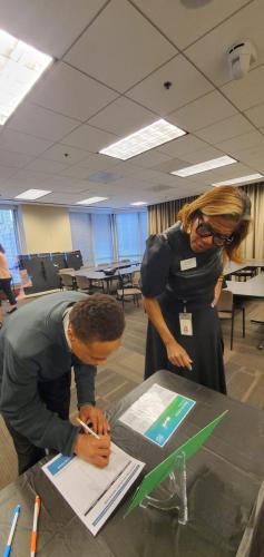 Two people in an office, one signing papers on a table while the other observes, exemplifying financial literacy.