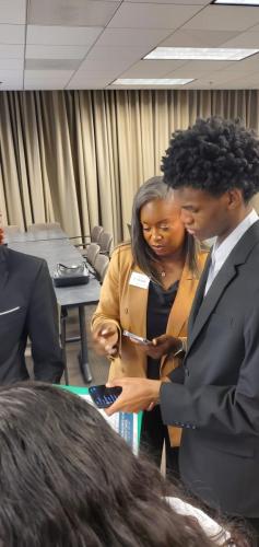Two people in formal attire discuss financial literacy while looking at a phone in a conference room.