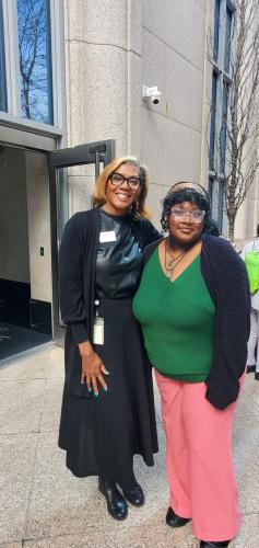 Two people standing and smiling in front of a building entrance, celebrating their journey to financial literacy success.