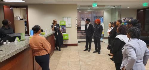 A group gathered in an office lobby, attentively listening to a woman speaking on financial literacy near the reception desk.
