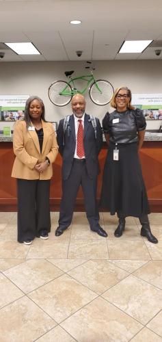 Three people smiling in an office lobby, highlighting financial literacy, with a green bike on the wall behind them.