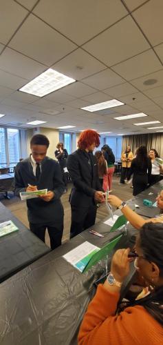 People engaging at a bustling event with tables and papers, fostering financial literacy in a conference room setting.