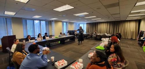 People seated at tables in a conference room, learning about financial literacy while enjoying Chick-fil-A boxes.