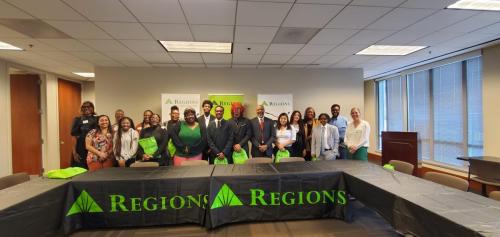 A group of people posing in a conference room with Regions banners, green gift bags, promoting financial literacy.