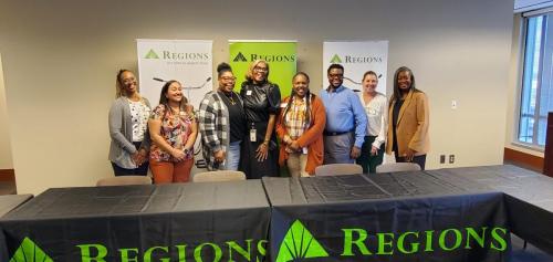 A group gathers before Regions banners, tables adorned with logos, promoting financial literacy.