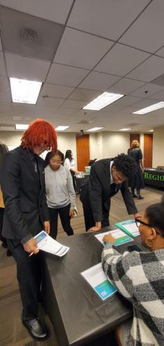 People attending a job fair, discussing financial literacy with representatives at a table in a conference room.