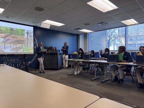 Students in uniforms present a project in a conference room with slides shown on a screen.