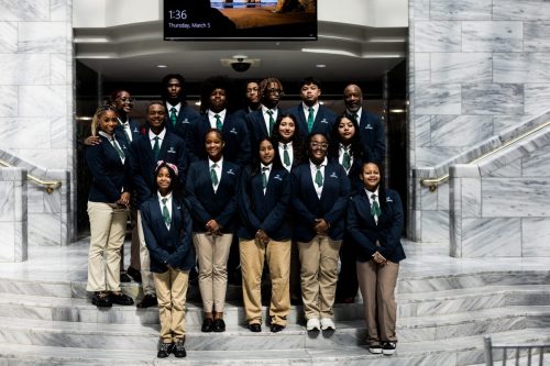 A group of people in matching blazers and khaki pants posing on marble stairs inside a building.
