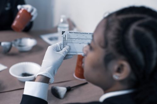 Person in gloves examines a document while sitting at a table with forensic tools and materials.