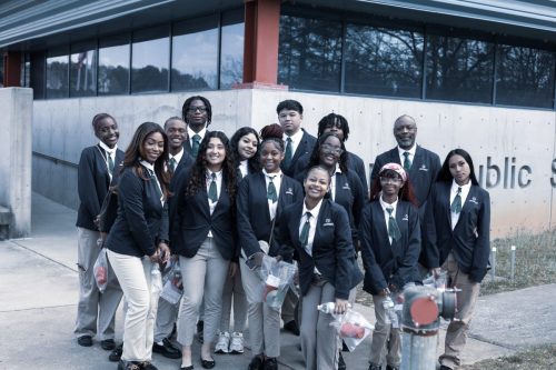 A group of students and adults in uniforms pose together outside a modern building.