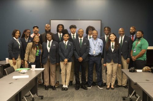 Group of people, some in blazers with green ties, pose and smile together in a conference room setting.